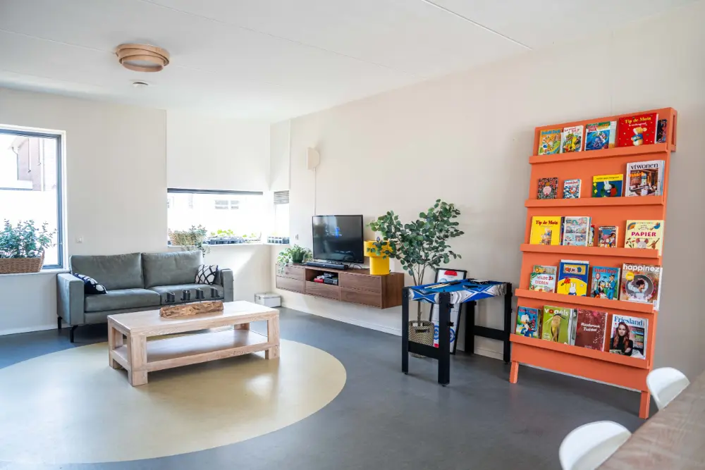 Lichte gemeenschappelijke woonkamer met een houten bank en een oranje boekenkast