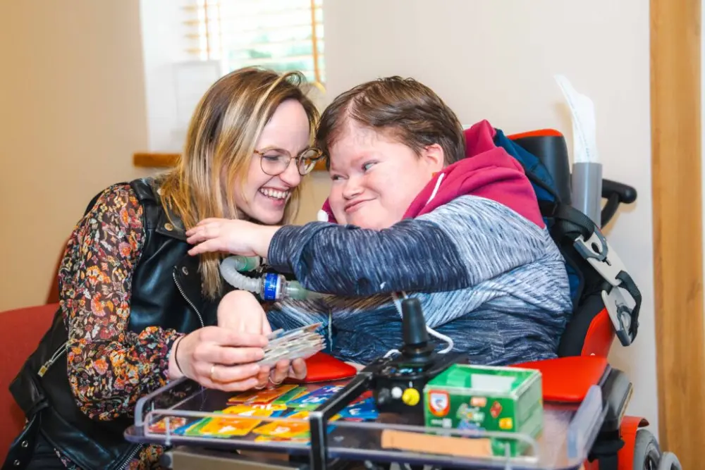 Een begeleider en een bewoner lachen samen tijdens een spel aan tafel