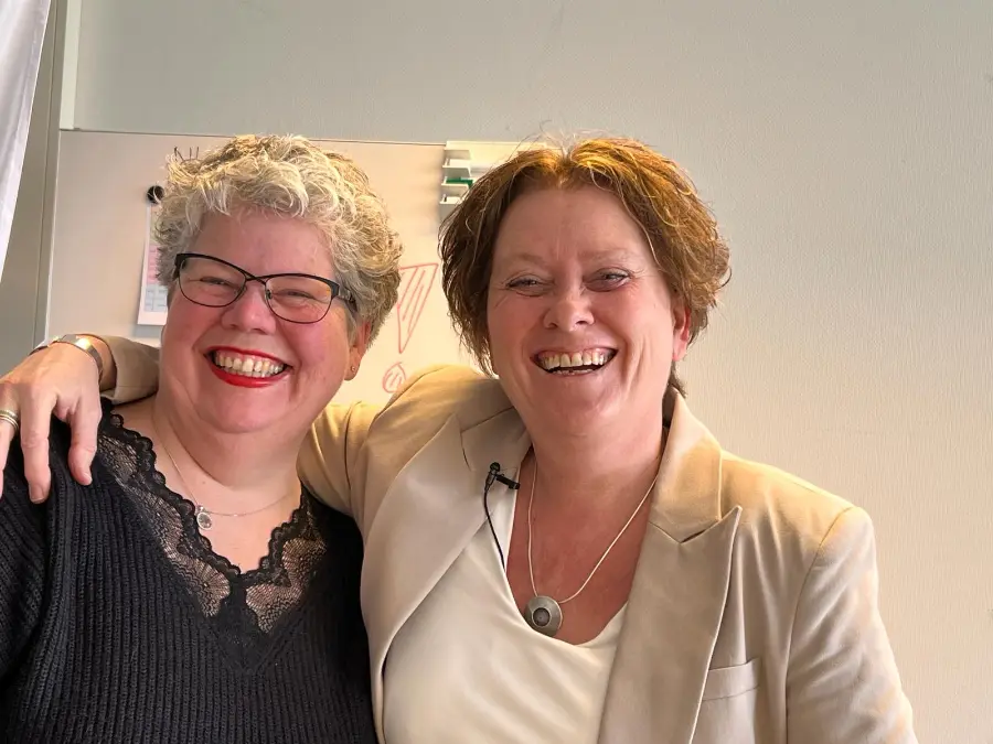 Twee vrouwen, een moeder en een collega, lachen samen naar de camera