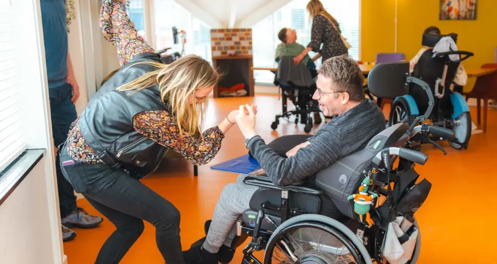 Een begeleider knielt bij een bewoner in een rolstoel in de oranje gang van locatie Bonkelaar