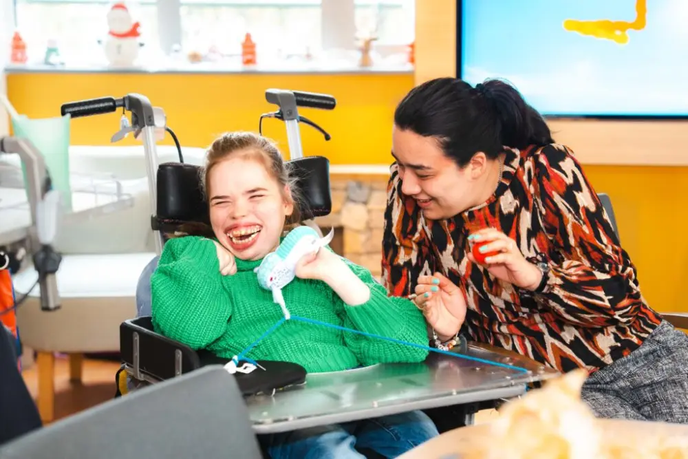 Een bewoner en een begeleider hebben samen plezier aan tafel in Villa Parkzicht