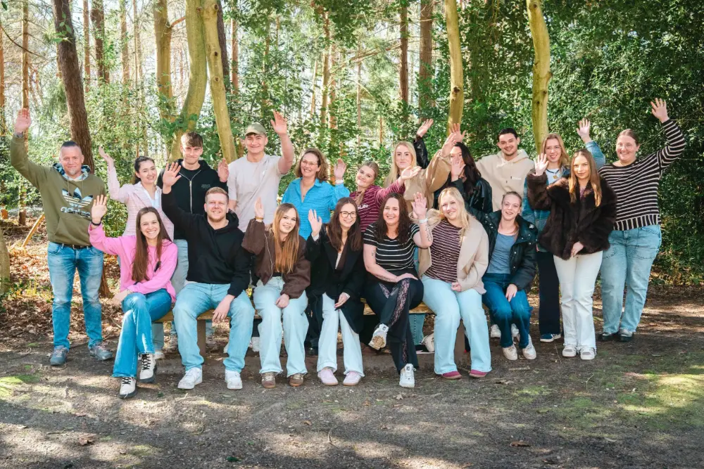 Grote groep collega's en leerlingen poseert vrolijk tussen de bomen tijdens de leerlingendag