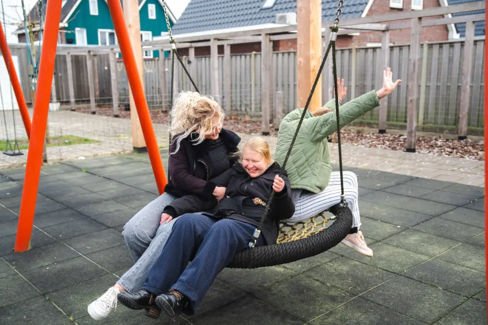 Een begeleider en een bewoner schommelen samen uitbundig in de tuin
